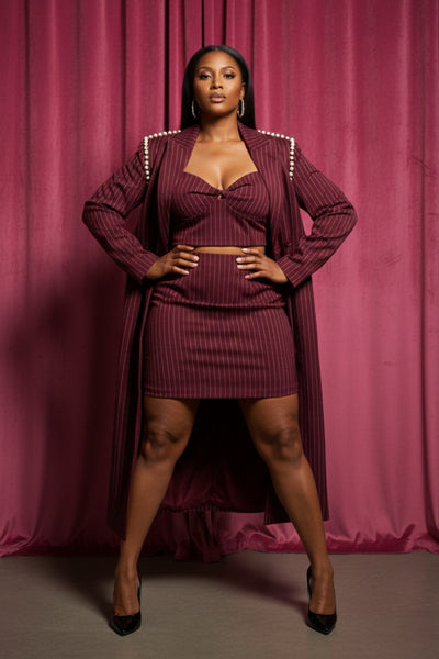 Woman wearing a maroon outfit with pearl embellishments against a pink curtain background