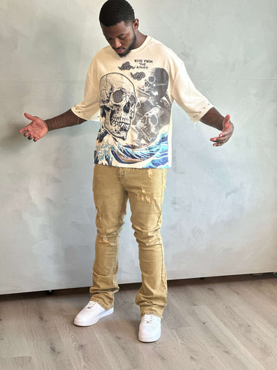 Man wearing a graphic t-shirt and beige pants standing against a plain wall.